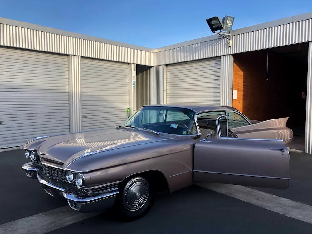 A classic car parked outside an open storage unit